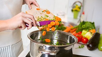Eine Frau schneidet Gemüse in den Kochtopf für eine gesunde Ernährung