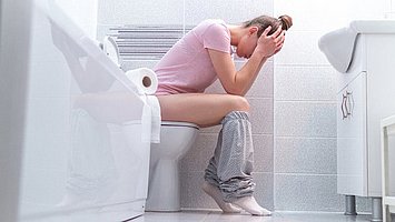 Frau sitzt mit Schmerzen aufgrund einer Blasenentzündung auf der Toilette