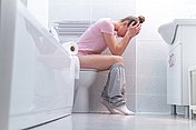 Frau mit Blasenentzündung auf der Toilette Frau sitzt mit Schmerzen aufgrund einer Blasenentzündung auf der Toilette