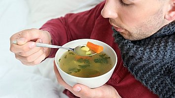 Ein Mann isst Hühnersuppe - diese ist bei Erkältungen immer noch ein bewährtes Hausmittel