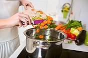 Gesundes Kochen Eine Frau schneidet Gemüse in den Kochtopf für eine gesunde Ernährung