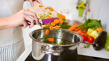 Eine Frau schneidet Gemüse in den Kochtopf für eine gesunde Ernährung