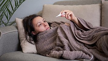 Fieber und oder erhöhte Temperatur: Eine Frau kontrolliert ihre Körpertemperatur mit einem digitalen Thermometer, um die Schwere ihrer grippalen Erkrankung zu beurteilen.